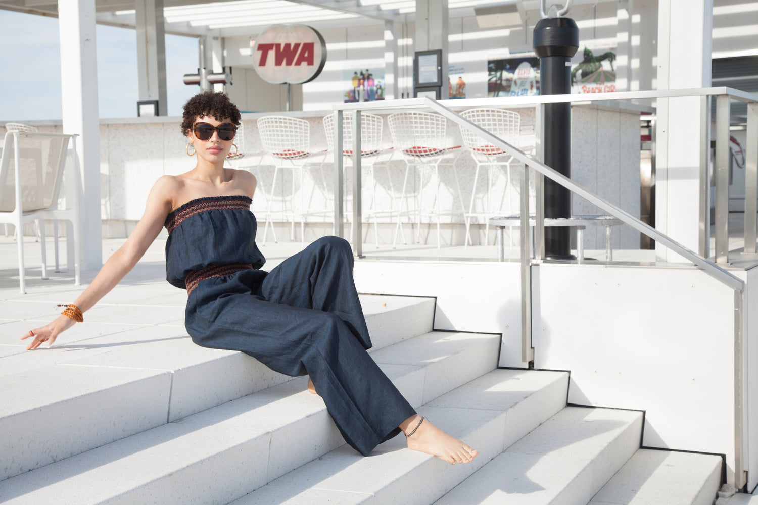 a woman in a romper is reclining on stairs by a rooftop bar