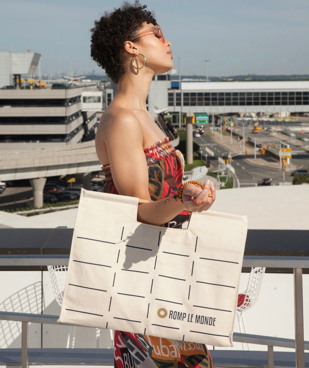 a woman holding a tote on an airport balcony